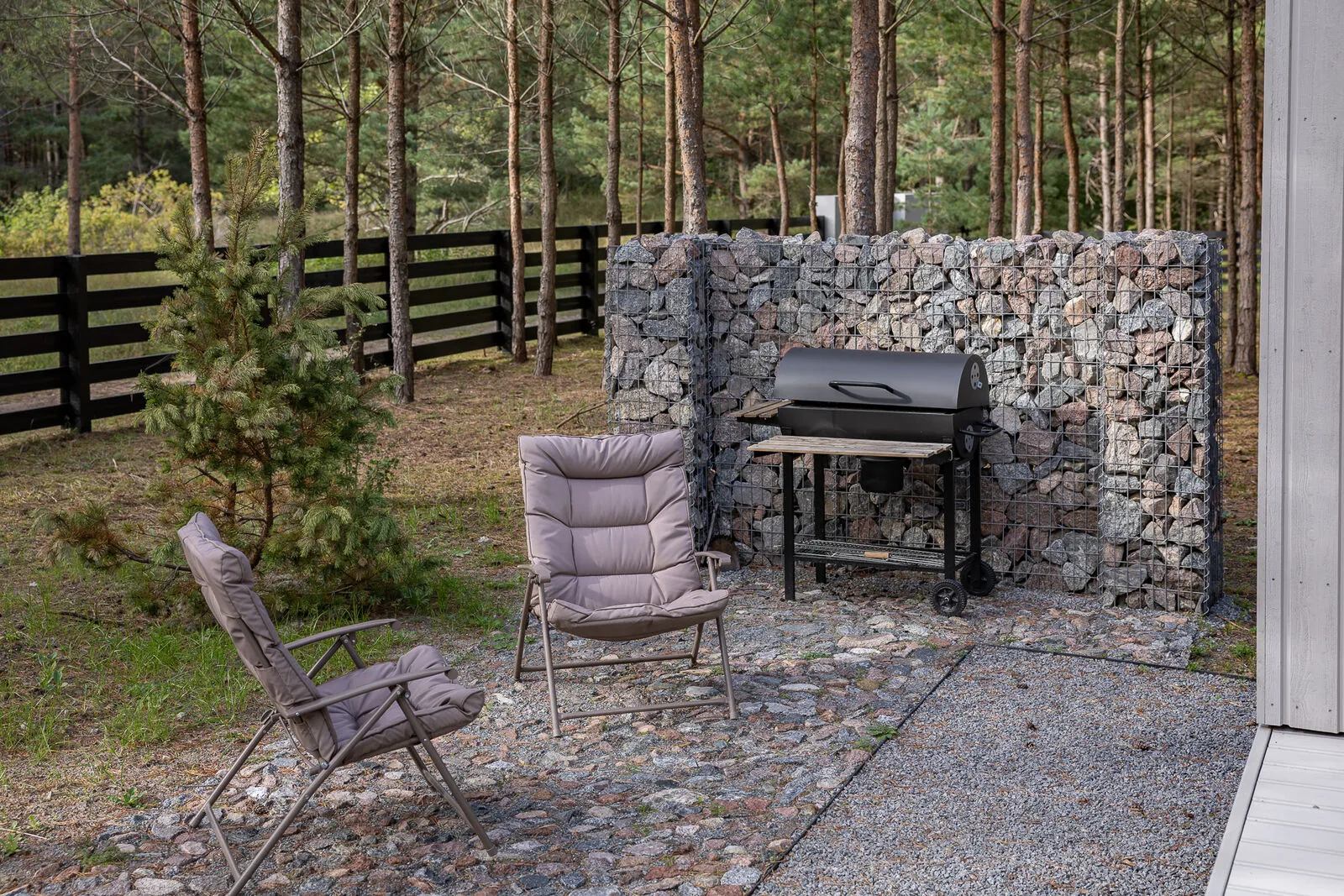 The grill and the lounge chairs behind the gabion wall